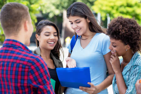 Laughing young hispanic female student talking with multi ethnic young adults outdoor in summer in cityの写真素材