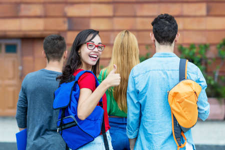 Laughing italian female student showing thumb up with group of other students at campus of universityの写真素材