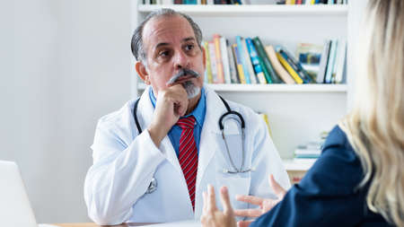 Hispanic male doctor listening to female patient at clinicの写真素材