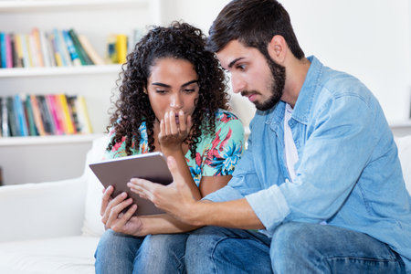 Latin american couple streaming video clips with tablet computer indoors at living room at homeの写真素材