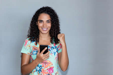 Cheering latin american adult woman with mobile phone with grey backgroundの写真素材