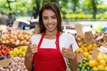 Beautiful brazilian farmers market seller with apron selling fruits outdoor in city in summerの写真素材