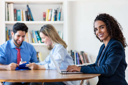 Latin American female software engineer working at computer with group of young business people at desk at officeの写真素材