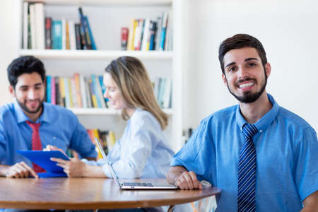 Portrait of brazilian businessman with group of latin american business people at desk at officeの写真素材