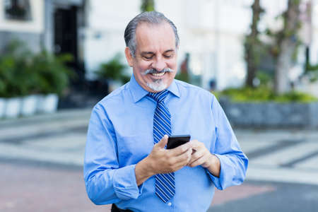 Latin american senior businessman starting video call with phone outdoor in city in summerの写真素材