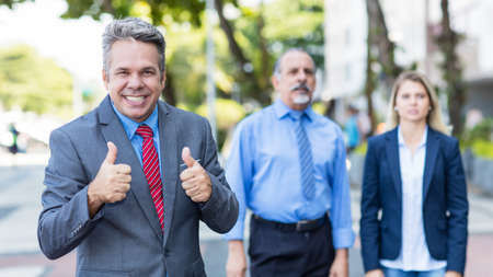 German mature businessman with colleagues showing thumbs up outdoor in city in summerの写真素材