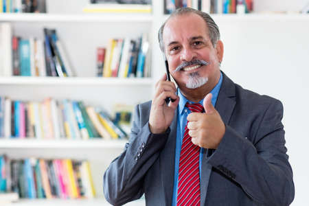 Hispanic senior businessman talking with client at phone at officeの写真素材