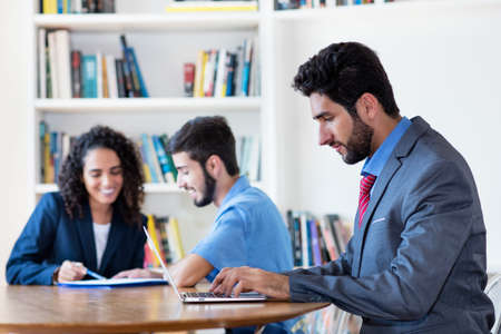 Hispanic software engineer working at computer with group of latin american business people at desk at officeの写真素材