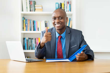 Smart african american mature businessman showing thumb up at desk at office of companyの写真素材
