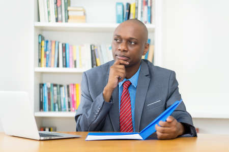 Thinking african american mature businessman with paperwork at desk at office of companyの写真素材