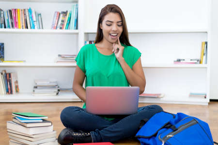 Laughing hispanic young adult female student watching online lecture at computer indoors at homeの写真素材
