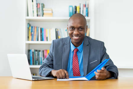 Laughing african american mature businessman working with paperwork at desk at office of companyの写真素材