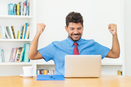 Cheering hispanic male trader at computerの写真素材