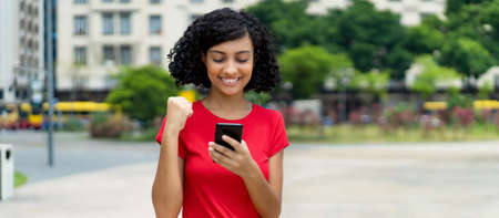 Arabic young adult woman receiving message with good news at mobile phone outdoor in summer in cityの写真素材