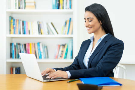 Hispanic mature businesswoman at video conference at computer at desk at officeの写真素材