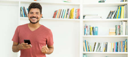 Happy mexican man receiving good news on mobile phone with copy space at homeの写真素材