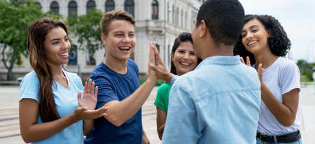 Multiethnic team of young adults give high five to friend outdoor in cityの写真素材