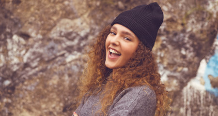Portrait of young adult woman with woolly hat and curly hair in urban styleの写真素材