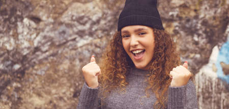 Cheering young adult woman with woolly hat and curly hair in urban styleの写真素材