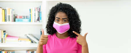 African american woman with pink face mask recommending protection against Covid-19 virusの写真素材