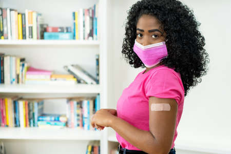 African american female young adult with plaster after vaccination against Covid-19 as symbol for coronavirus injectionの写真素材