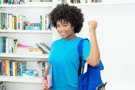 Cheering african american female student with blue shirt at classroom of universityの写真素材