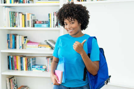 African american female student with blue shirt showing thumb up at classroom of universityの写真素材