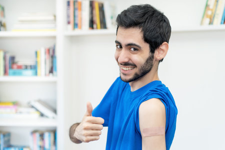 Arabic man showing thumb up after third vaccination against Covid 19 as protection against coronavirusの写真素材