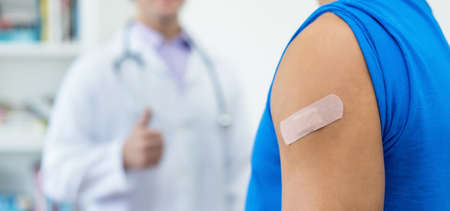 Plaster on arm of man and thumb up of doctor after third vaccination against Covid 19 as protection...