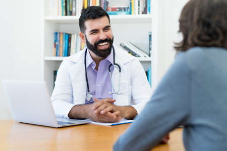Handsome mature doctor with hipster beard talking with healthy patient at office of hospitalの写真素材
