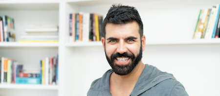 Portrait of laughing hispanic mature adult man with beard indoors at homeの写真素材