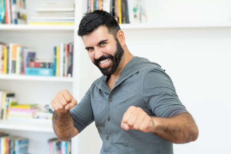 Cheerful hispanic mature adult man with beard indoors at homeの写真素材