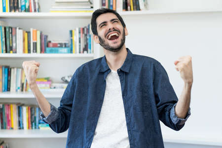 Excited cheering arabic man with beard indoors at homeの写真素材