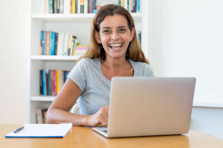 Laughing mature adult female teacher working at computer at home or at officeの写真素材
