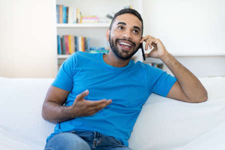 Handsome latin american hipster man with beard flirting at mobile phone indoors at homeの写真素材