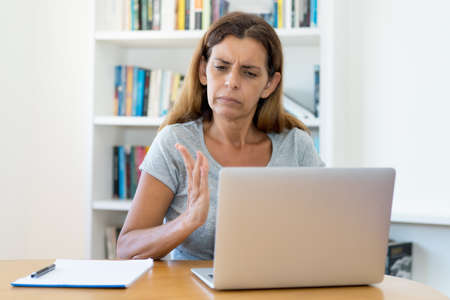 Mature adult female teacher in discussion with students at online lecture at computer at home or at officeの写真素材
