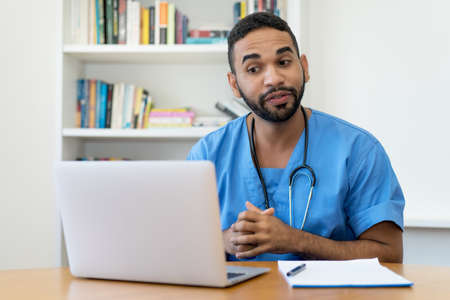 Handsome latin american male nurse talking with patient at computer at hospitalの写真素材
