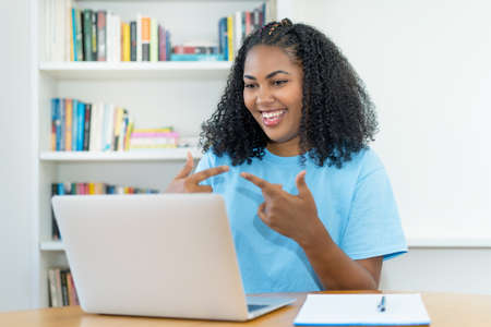 Latin american female student talking at online lecture at desk indoors at homeの写真素材