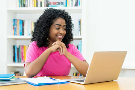 Brazilian young adult watching movie at computer at desk indoors at homeの写真素材