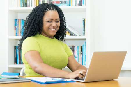 Laughing african american female student working at computer indoors at homeの写真素材