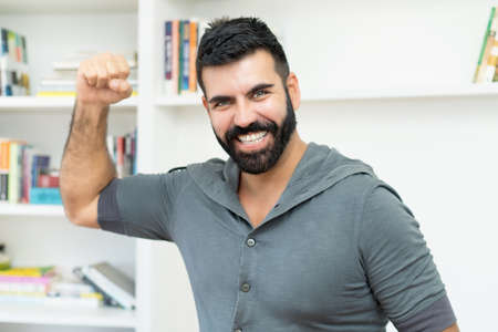 Cheering hispanic mature adult man with beard indoors at homeの写真素材