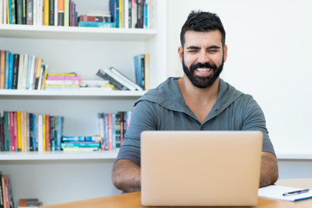 Laughing latin american man with hipster beard at computer at officeの写真素材