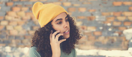 Beautiful latin american female young adult with knit hat talking on phone outdoor in urban city styleの写真素材