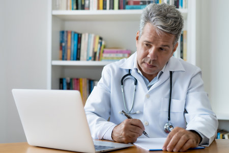 Oncologist reading studes about cancer and working at computer at office of hospitalの写真素材