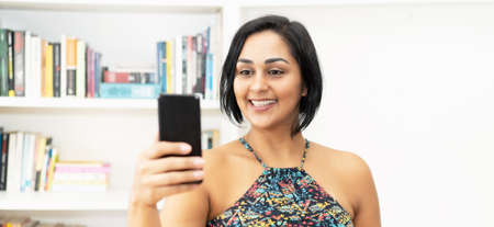 Mexican mature adult woman streaming clip online with phone indoors at homeの写真素材