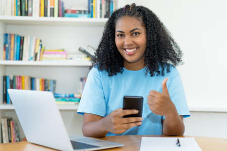 Laughing latin american woman writing message at phone indoors at homeの写真素材