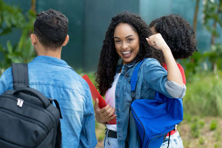 Cheering hispanic female student with braces and group of young adults at campus of universityの写真素材