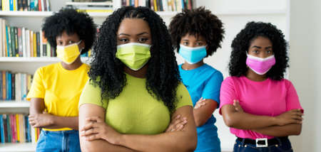 Pretty african american woman with green face mask and group of female young adults recommending protection against Covid-19 virusの写真素材