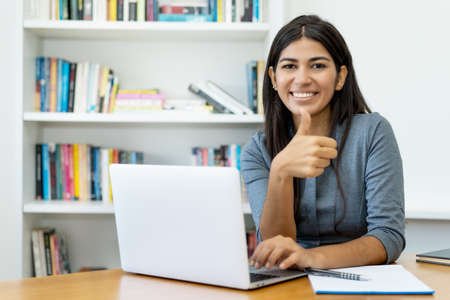 South american woman at computer showing thumb up at officeの写真素材