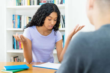 Pretty latin american female student learning with teacher on private lessons at desk at classroomの写真素材